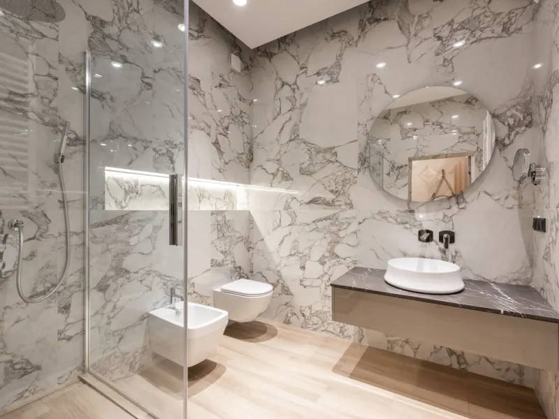 A finished bathroom with marble walls and a glass shower