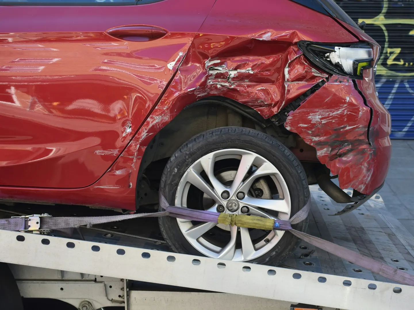 A damaged red car strapped down on a flatbed