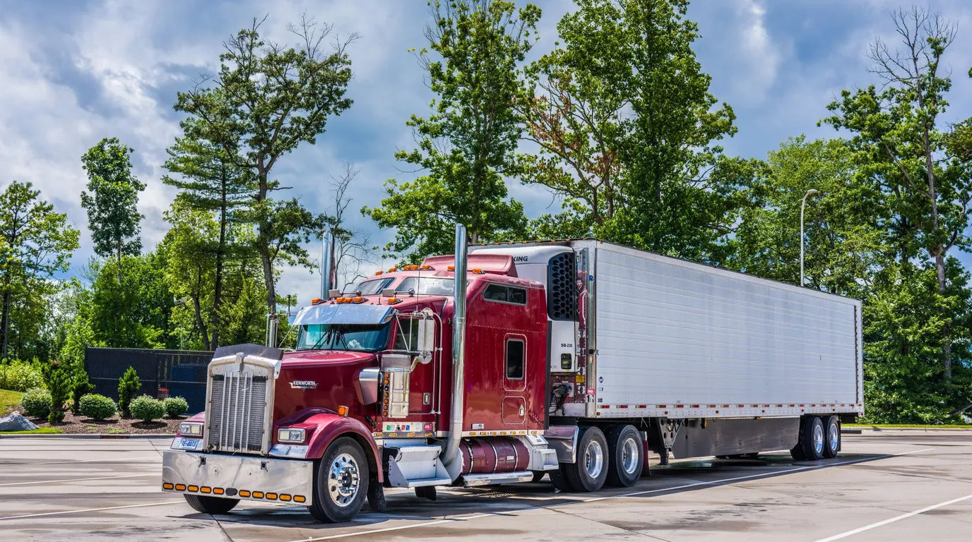 A red semi truck parked in a lot lined with trees